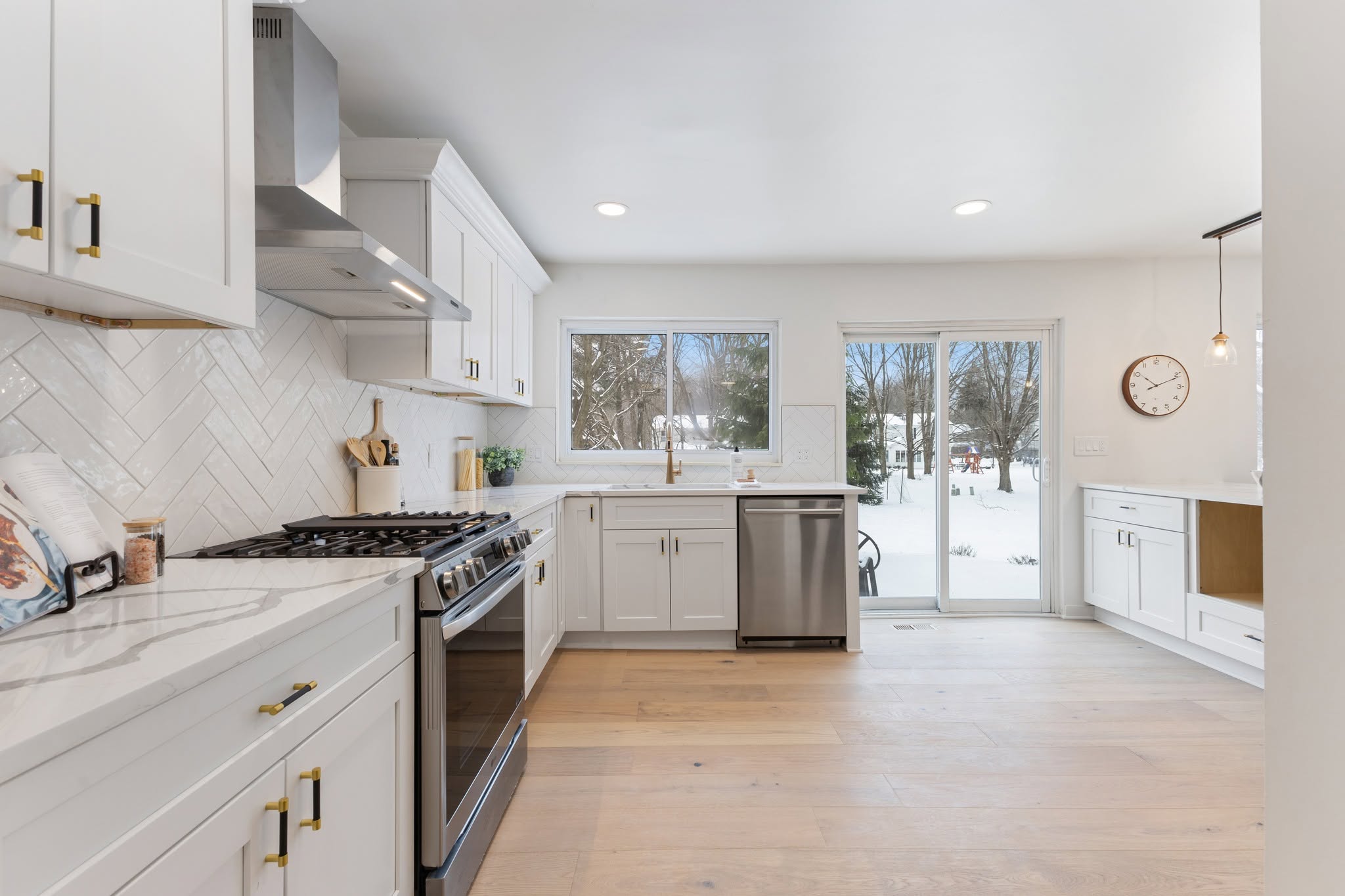 Bright white Shaker kitchen cabinetry with pale wood flooring and a garden view