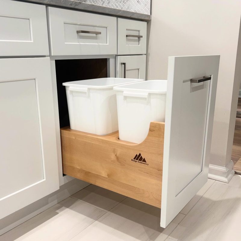 Open white Shaker cabinet with a wood pull-out drawer holding two waste bins