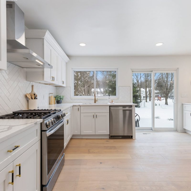 Bright white Shaker kitchen cabinetry with pale wood flooring and a garden view